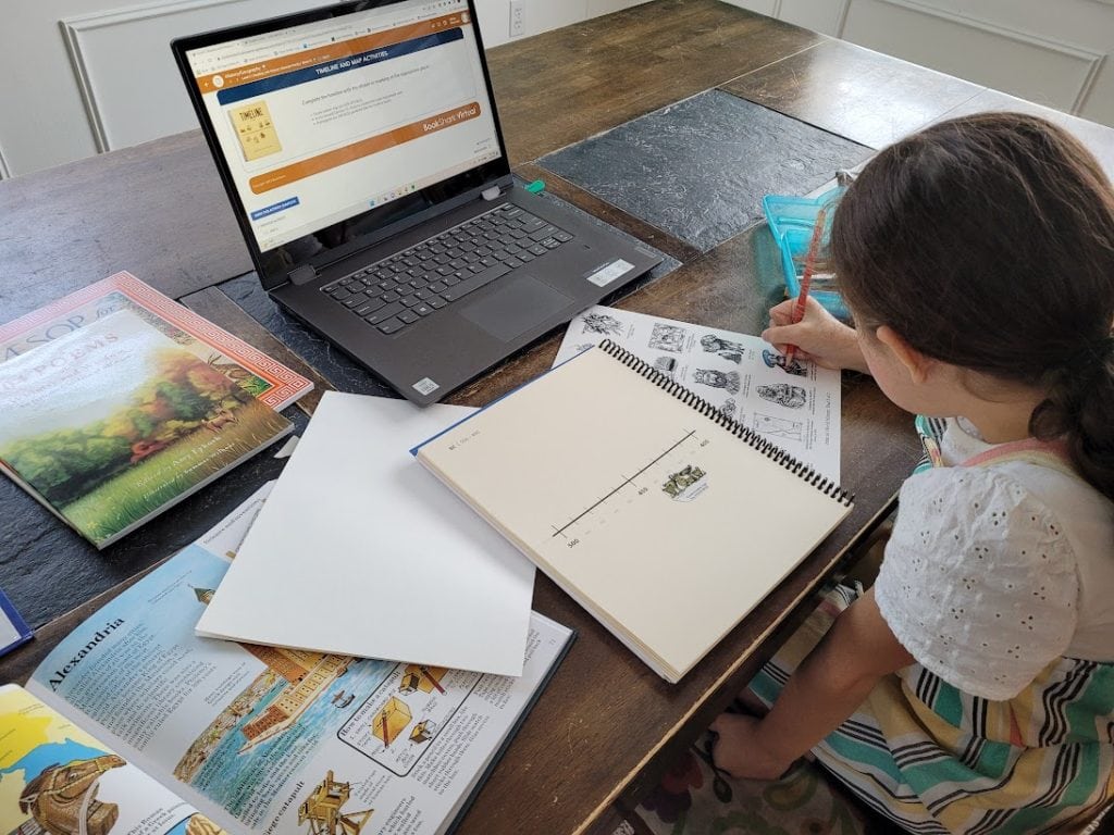 little girl at table with history books coloring timeline figure for her timeline notebook