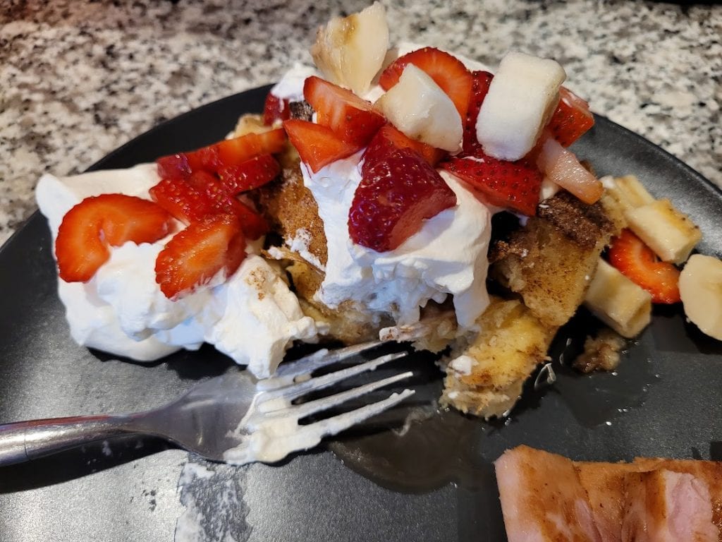 plate of french toast casserole with whipped cream, strawberries and bananas 