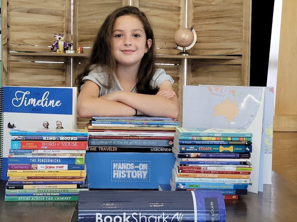 Olivia standing by her huge pile of Bookshark curriculum for the year