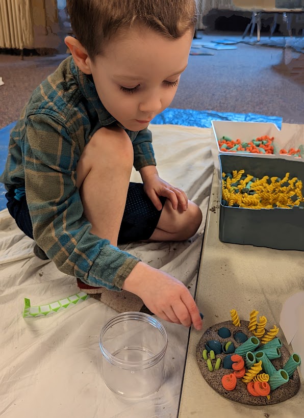 Pre-K boy playing with ocean habitat made from playdough sand and colored pasta